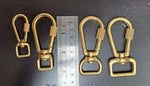 Four gold metal swivel hooks with a ruler for scale on a dark surface