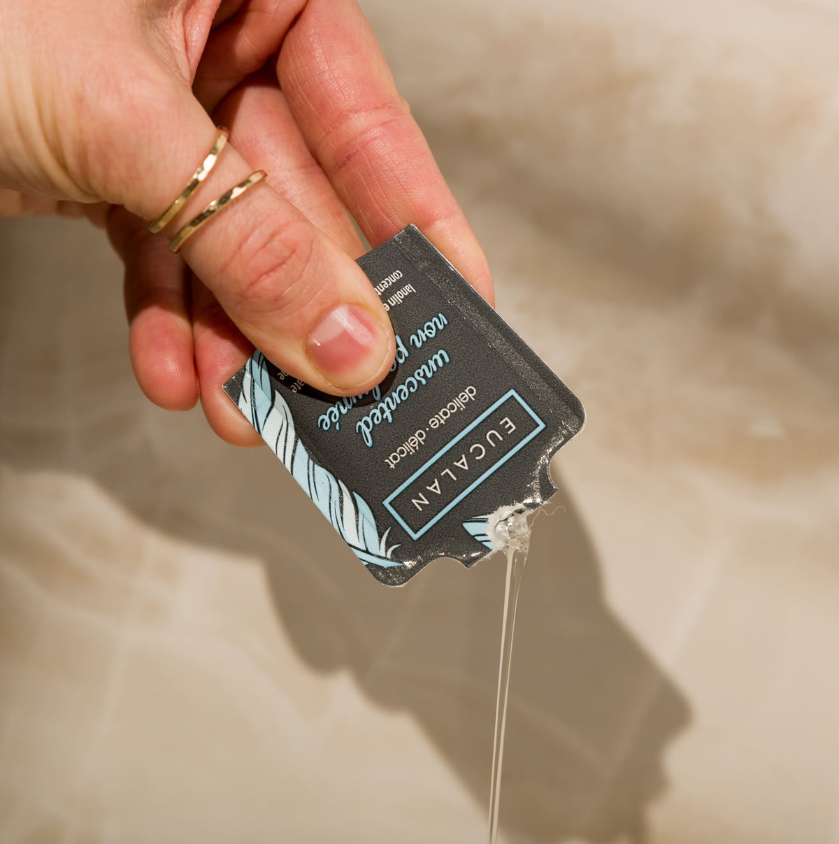 Hand holding a small container of Eucalan product with a beige background