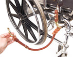 Close-up of a wheelchair with a quick release wheelchair leash attached, a person's hand is holding the end of the leash