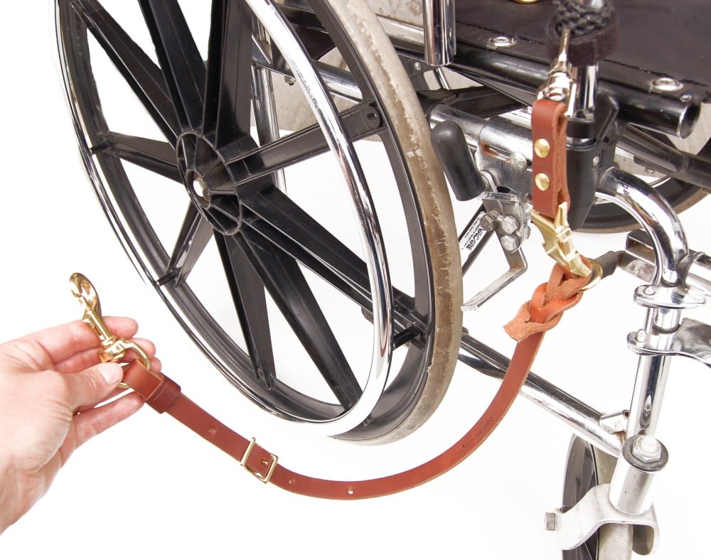 Close-up of a wheelchair with a quick release wheelchair leash attached, a person's hand is holding the end of the leash
