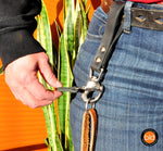 Person in jeans wearing a shackle snap belt loop standing next to a plant on an orange background.