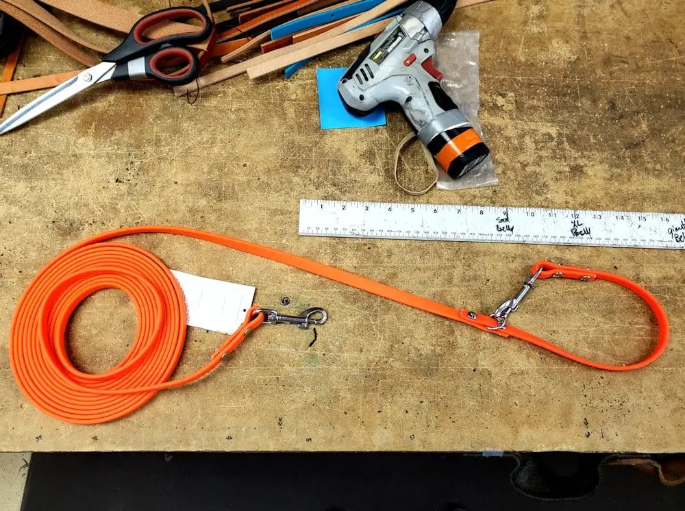 Orange leash on a wooden workbench with tools including scissors, a driver, and a ruler.