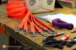 Orange dog leashes with silver clasps on a wooden table with tools and supplies.