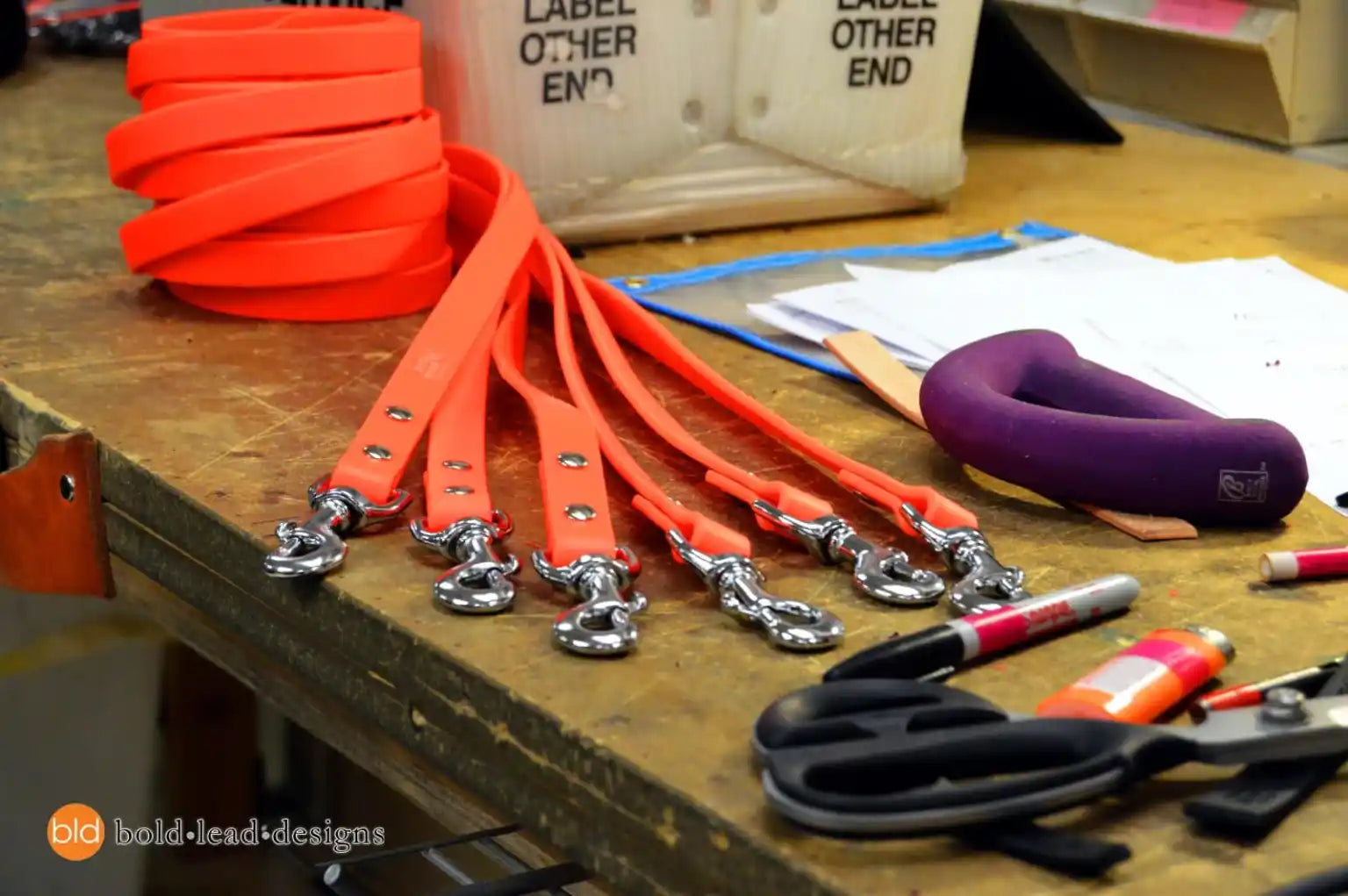 Orange dog leashes with silver clasps on a wooden table with tools and supplies.