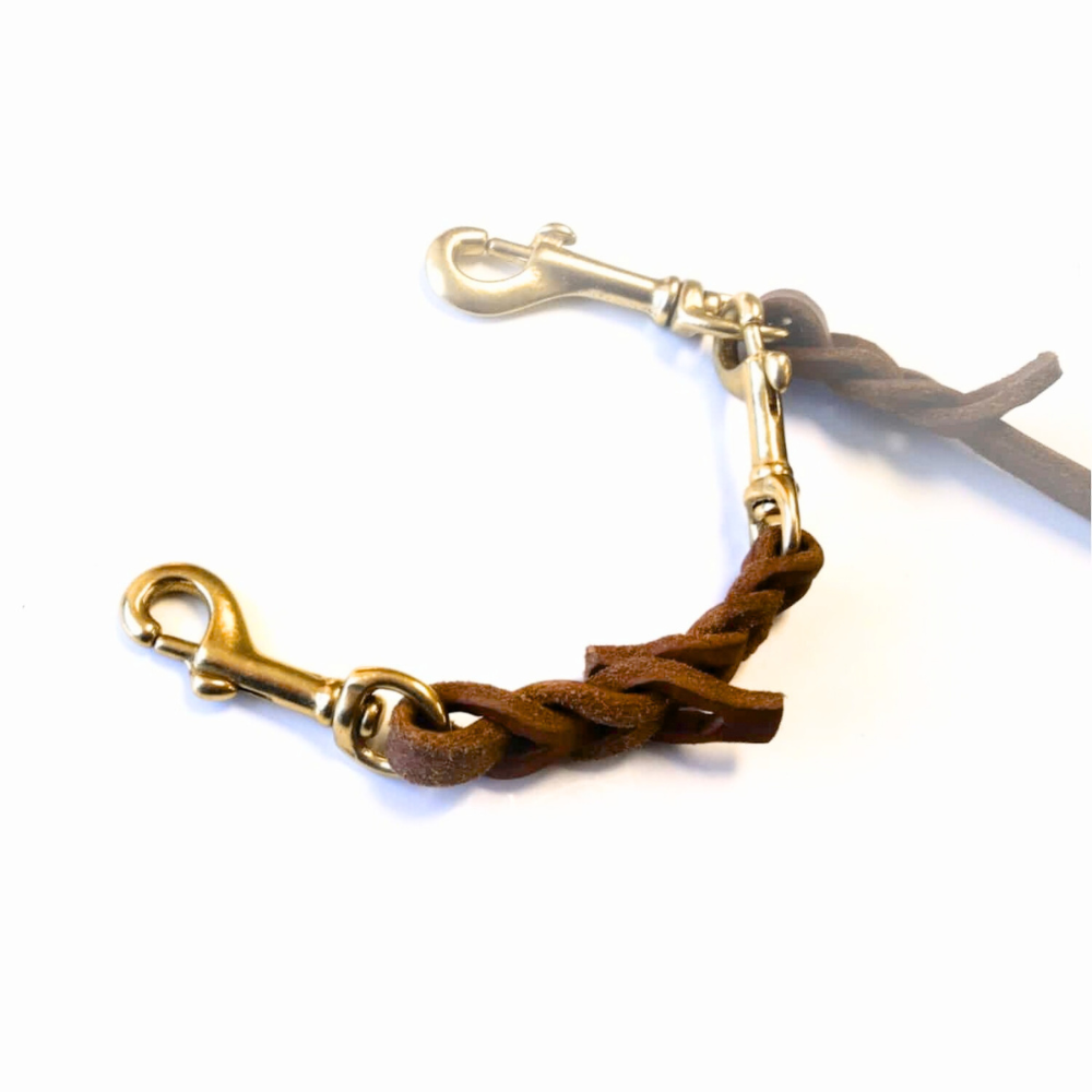 tan and brass braided leather safety cord on a white background shown clipped to a leash that is faded into the background