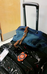 Blue suitcase tethered to a black suitcase with a tan leather leash caddy