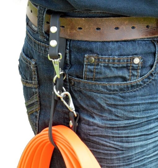 A close up of a person's hip with the brahma leash caddy connected to the belt and an orange leash